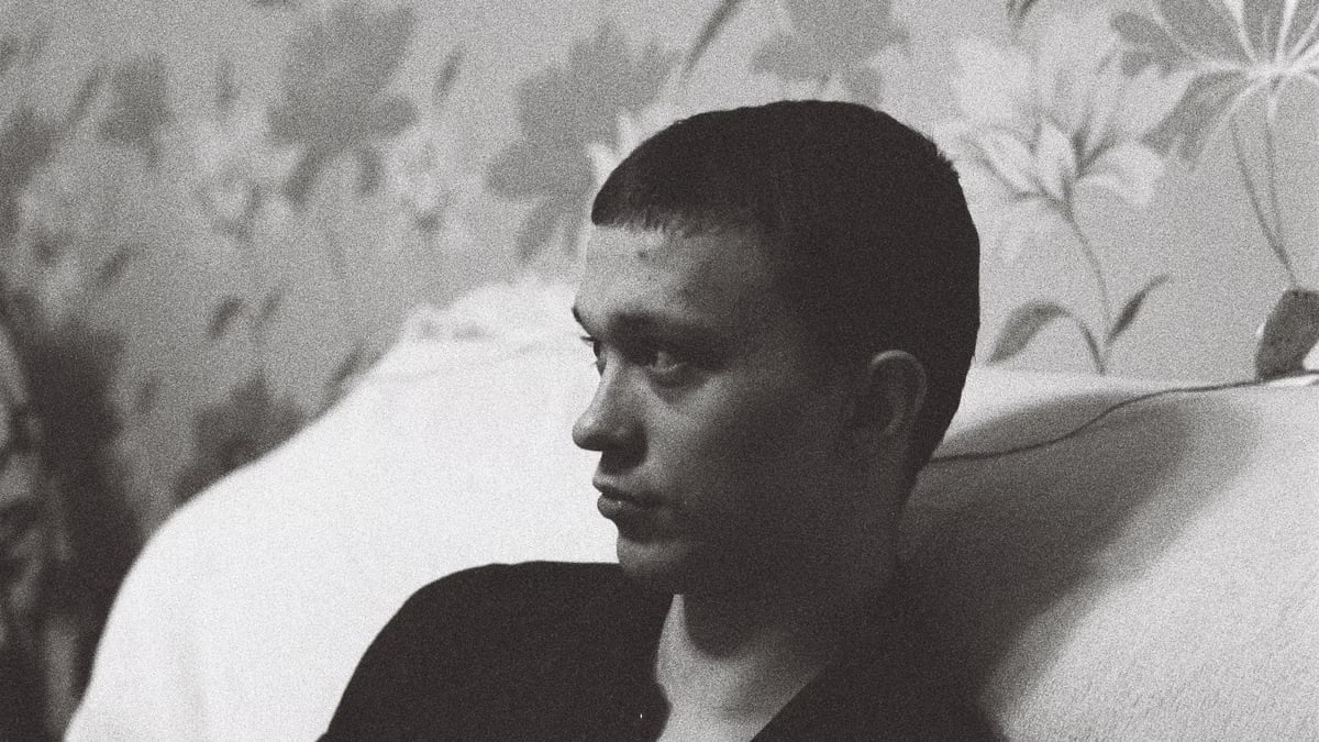 A man leans on a sofa, deep in thought, captured in striking black and white.